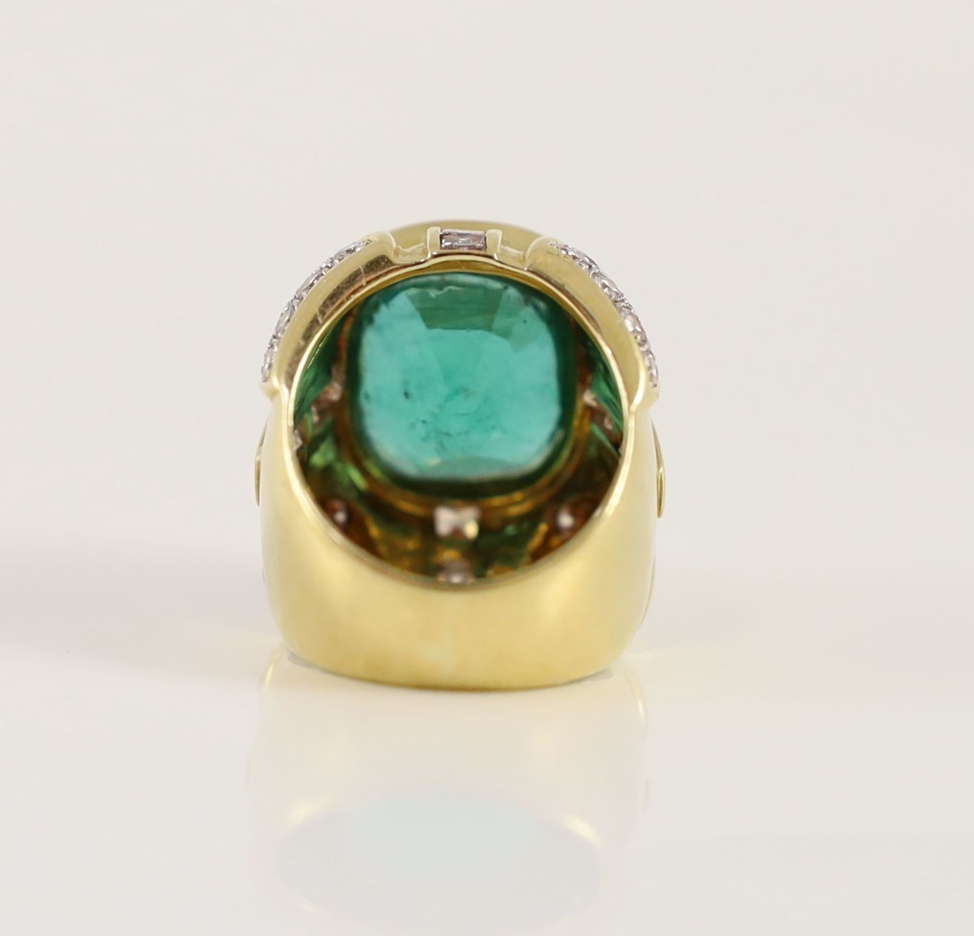 A large gold and single stone oval cut emerald set dress ring, with round and princess cut diamond cluster set shoulders